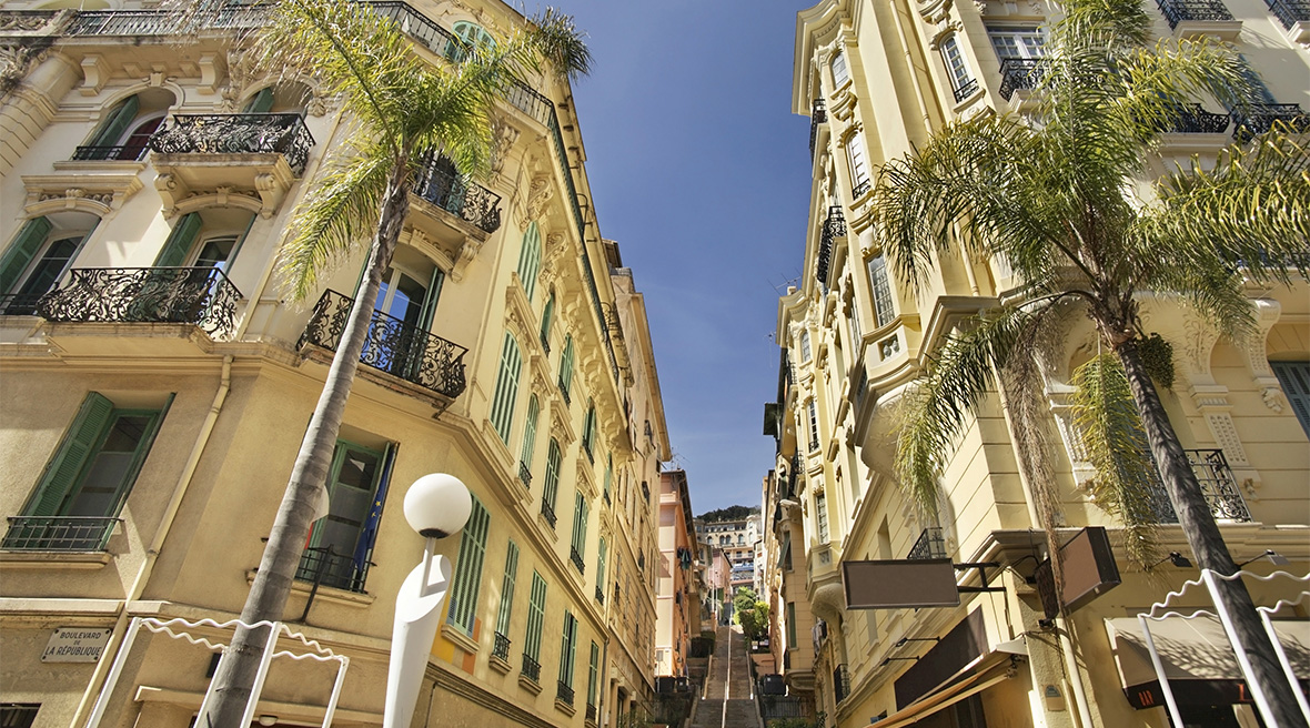 a long road stretching uphill with two decorative buildings each side with palm trees and balconies